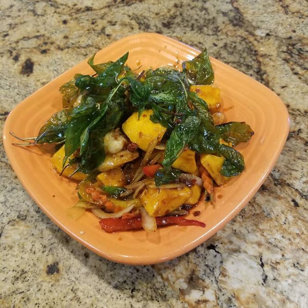 Thai stir-fry with yellow squash, red peppers, onions, and basil on an orange plate.