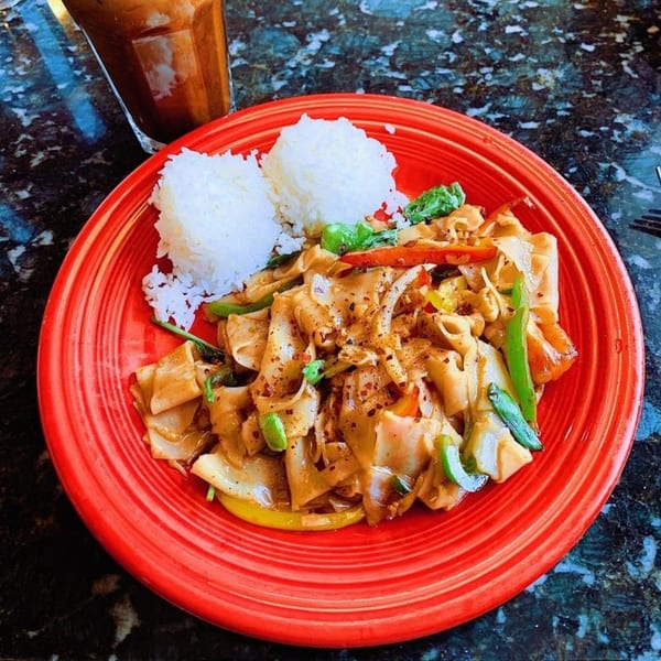 Thai drunken noodles with rice and a drink on a red plate at House of Noodle.