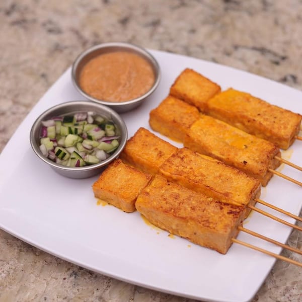 Thai tofu satay skewers with peanut sauce and cucumber relish on a white plate.