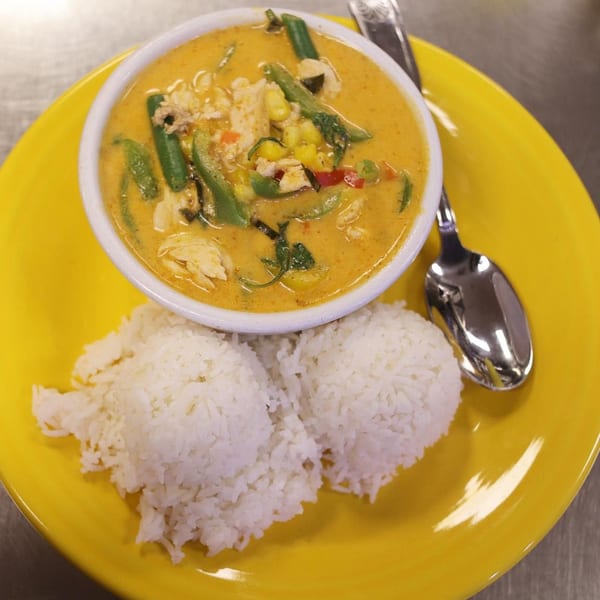 Thai red curry with chicken, vegetables, and two scoops of white rice on a yellow plate.