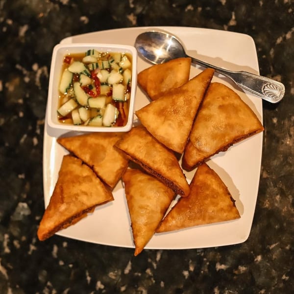 Golden fried wontons with a side of cucumber relish and a spoon on a white plate.