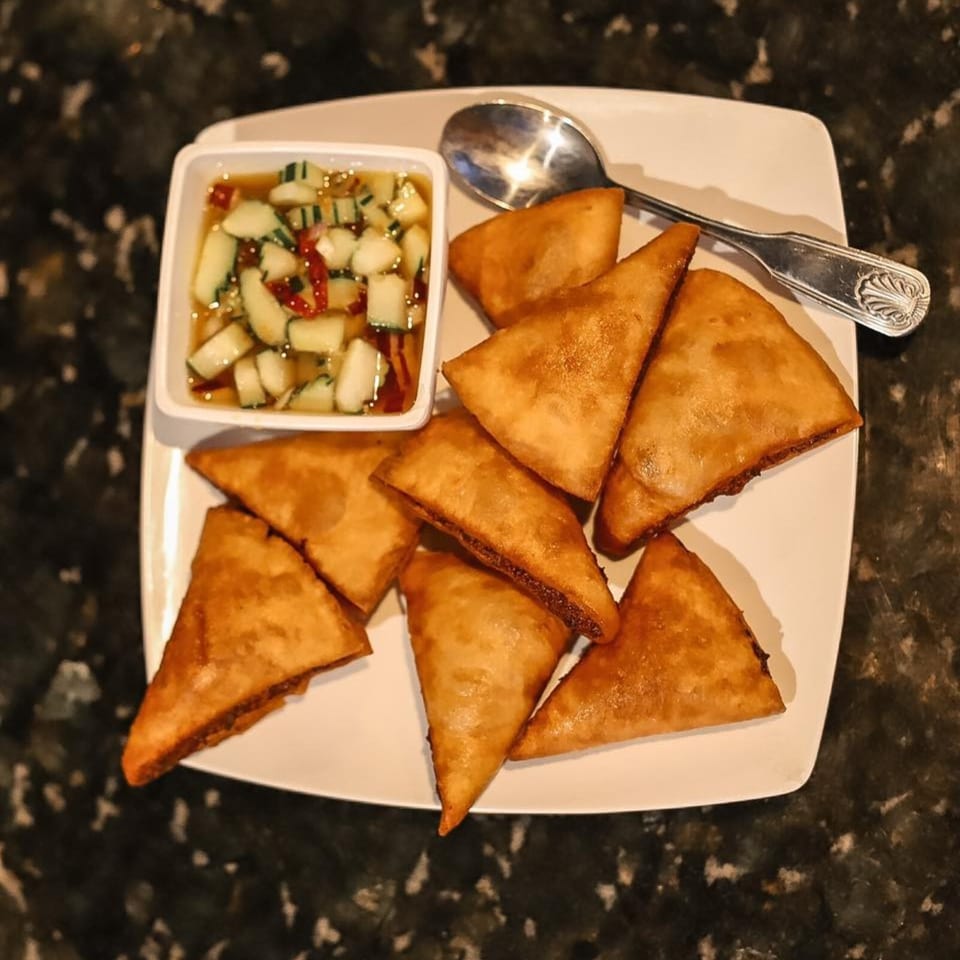 Golden fried wontons with a side of cucumber relish and a spoon on a white plate.
