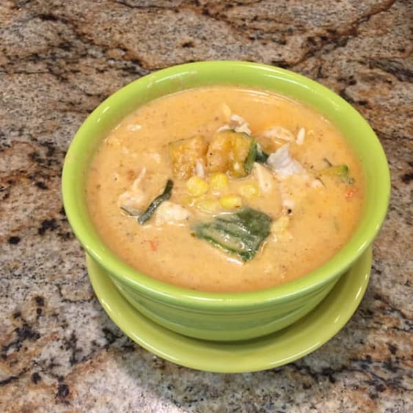 Creamy Thai soup with corn, tofu, and green vegetables in a vibrant green bowl.