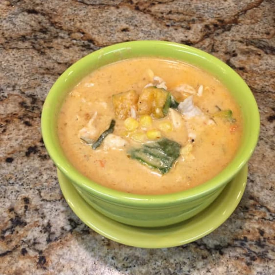 Creamy Thai soup with corn, tofu, and green vegetables in a vibrant green bowl.